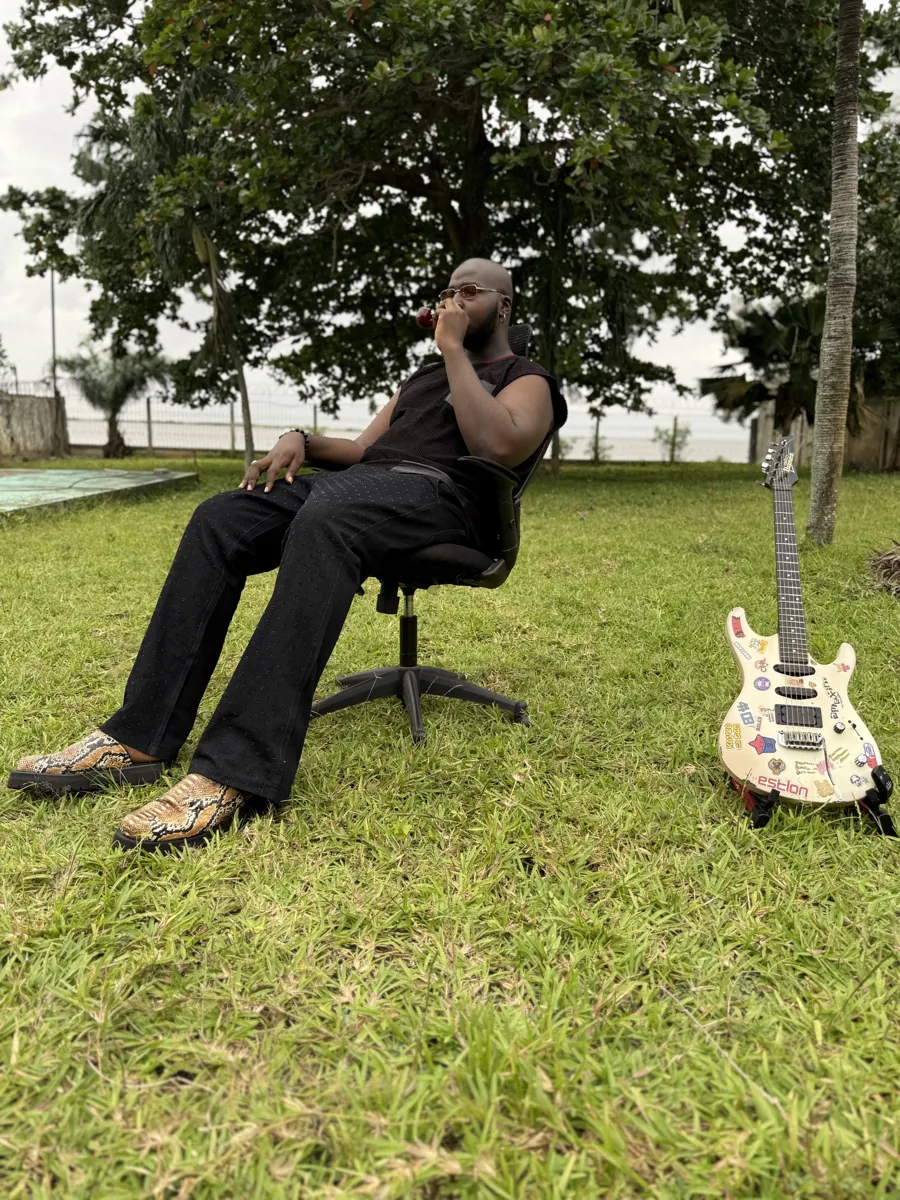 CJ Obassey sitting in a garden with his sticker-covered guitar beside him
