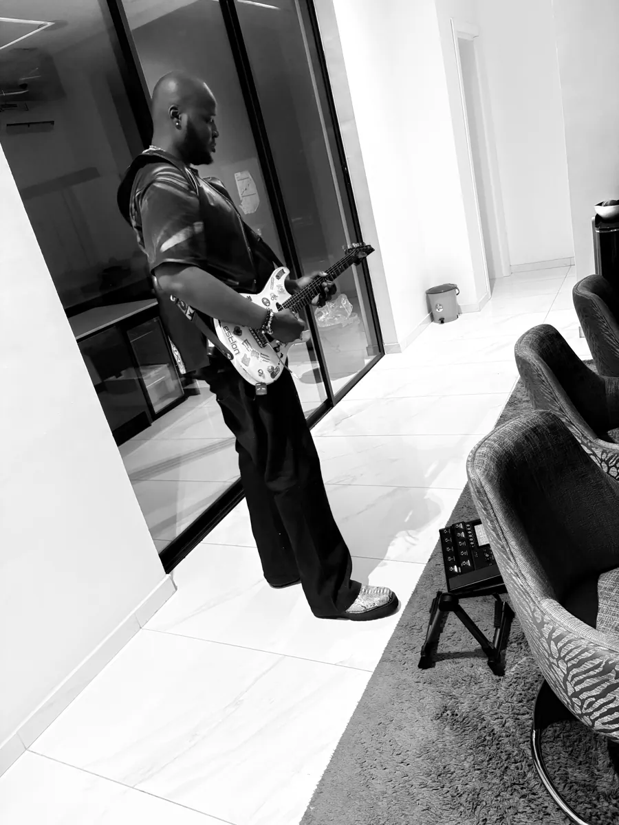 CJ Obassey playing electric guitar in a lounge, black and white