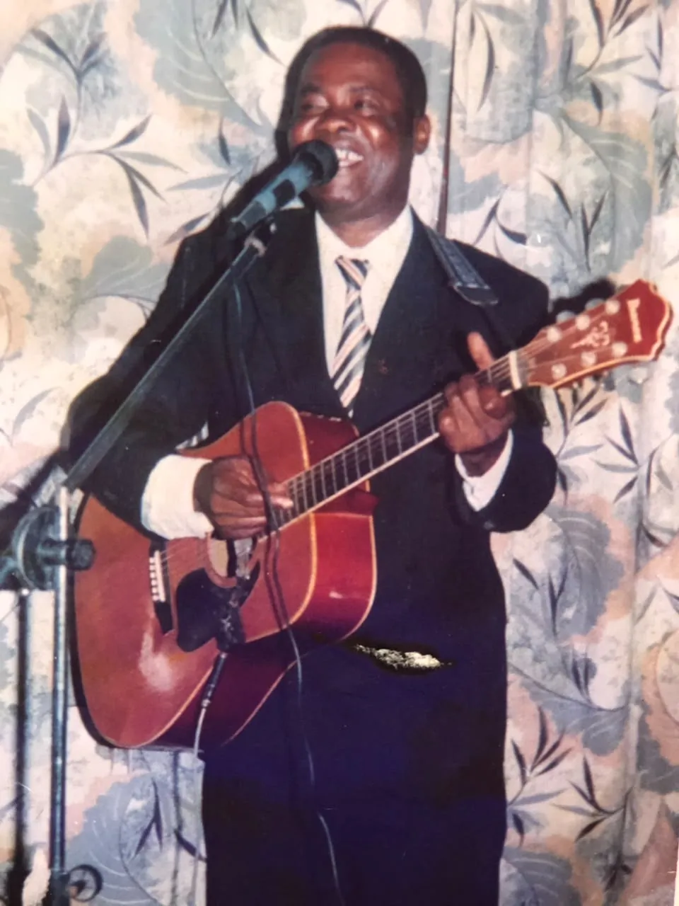 Rev. Patty Obasi singing with his acoustic guitar